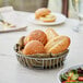 A round chrome wire basket filled with bread rolls and salad on a table.