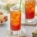 A table with a glass of Davidson's Organic Ceylon Black Iced Tea with a straw and ice, and a green pastry.