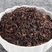 A bowl of Davidson's Organic Spiced Raspberry loose leaf tea with black tea leaves and red and purple flowers.