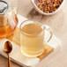 A glass mug of Davidson's Organic Autumn Fruit and Flowers herbal tea on a cutting board with a teapot.