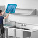 A man in a blue shirt using a Regency wall mounted shelf over a stainless steel sink.