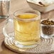 A glass mug of Davidson's Organic White Spicy Peach Tea on a table next to a bowl of dried herbs.