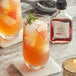 A glass of orange Runamok Maple Bitters drink with ice and a rosemary sprig next to a bottle of Runamok Maple Bitters.