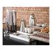 An Abert Cosmo stainless steel coffee urn on a table with coffee cups and bowls.