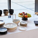 An Abert Cosmo stainless steel round platter on a table with plates and bowls.