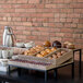 A table with an Abert Revolution riser set displaying pastries and coffee cups.