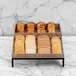 A table with an Abert Revolution riser set holding trays of bread and cookies.