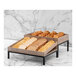 Two Abert Revolution display risers with trays of food on a table in a bakery.