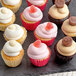 A group of Sweet Street Desserts assorted cupcakes with white, pink, and candy toppings on a slate.