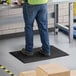 A person wearing blue jeans standing on a Choice black anti-fatigue floor mat.