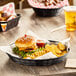 A Carlisle black plastic serving basket on a table with a cheeseburger and fries.