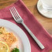 A Oneida Chef's Table stainless steel dinner fork on a napkin next to a plate of food.