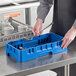 A person holding a blue tray with a round lid on a counter in a school kitchen.