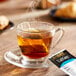 A glass cup of Bigelow Earl Grey tea with a tea bag in it on a saucer.