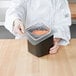 A person in a white coat holding a Cambro clear flat pan lid filled with carrots.