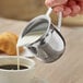 A person using a Choice stainless steel bell creamer to pour milk into a cup of coffee.