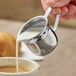 A person using a Choice stainless steel bell creamer to pour milk into a cup of coffee.