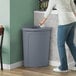 A woman in a hospital cafeteria standing next to a Lavex corner round trash can with a gray rim top.