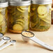 A Ball jar of pickles next to a white measuring spoon filled with pickle mix.