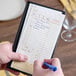 A tan and white carbonless guest check with beverage lines and a bottom guest receipt, held in a black holder and being written on with a blue pen.