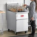 A woman using tongs to fry food in an Avantco liquid propane floor fryer.