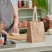 A woman using a brown paper bag with handles to make a Choice brown paper bag with a customizable label.