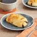 A plate with a Bridor Ready to Bake Butter Pain Au Chocolate pastry on it next to a cup of coffee.