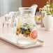 A Libbey glass pitcher of water with fruit and ice on a tray.