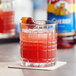 A glass of liquid with a cherry and Torani Cherry Flavoring Syrup on a table.