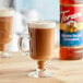 A glass cup of brown coffee next to a bottle of Torani Brown Sugar Cinnamon flavoring syrup.