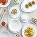 A table set with Acopa Cordelia bright white porcelain bowls, plates, and cups.