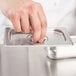 A hand using a Vollrath Super Pan V stainless steel lid to cover a metal tray.