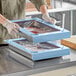A person using blue Pan Stackers to hold a tray of food in a professional kitchen.
