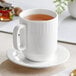 An Acopa Cordelia white porcelain mug on a saucer with brown liquid in it.