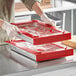 A gloved hand uses a red Pan Stackers container to wrap a tray of food.