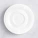 An Acopa Cordelia bright white porcelain saucer with an embossed circle on a white surface.