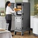 A woman in a kitchen putting food into a Cambro Pro Cart Ultra pan carrier.