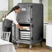 A woman using a Cambro Pro Cart Ultra to put food into a large metal container.