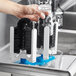 A person using a KissKleen manual glass washer brush to clean glassware over a sink in a professional kitchen.