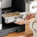 A person using a Vollrath stainless steel steam table pan to cook food in an oven.