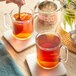 A person pouring David Rio Masala Chai into two cups on a table.