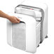 A person's hand using a Fellowes Powershred LX200 white micro-cut shredder.