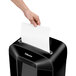A hand putting a white sheet of paper into a black Fellowes LX85 paper shredder.