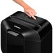 A hand pressing a button on a black Fellowes Powershred LX25 paper shredder.