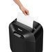 A hand putting a piece of paper into a Fellowes Powershred LX25 paper shredder.