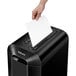 A hand putting a piece of paper into a Fellowes Powershred LX65 paper shredder.