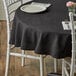 A table with a black Choice 100% Spun Polyester Hemmed Cloth Table Cover and a white chair.