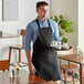 A man wearing a Choice black bib apron holding a tray of coffee cups on a counter in a professional kitchen.