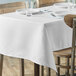 A white rectangular table cloth on a table with plates and glasses.