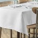 A white rectangular table cover with plates and glasses on it.